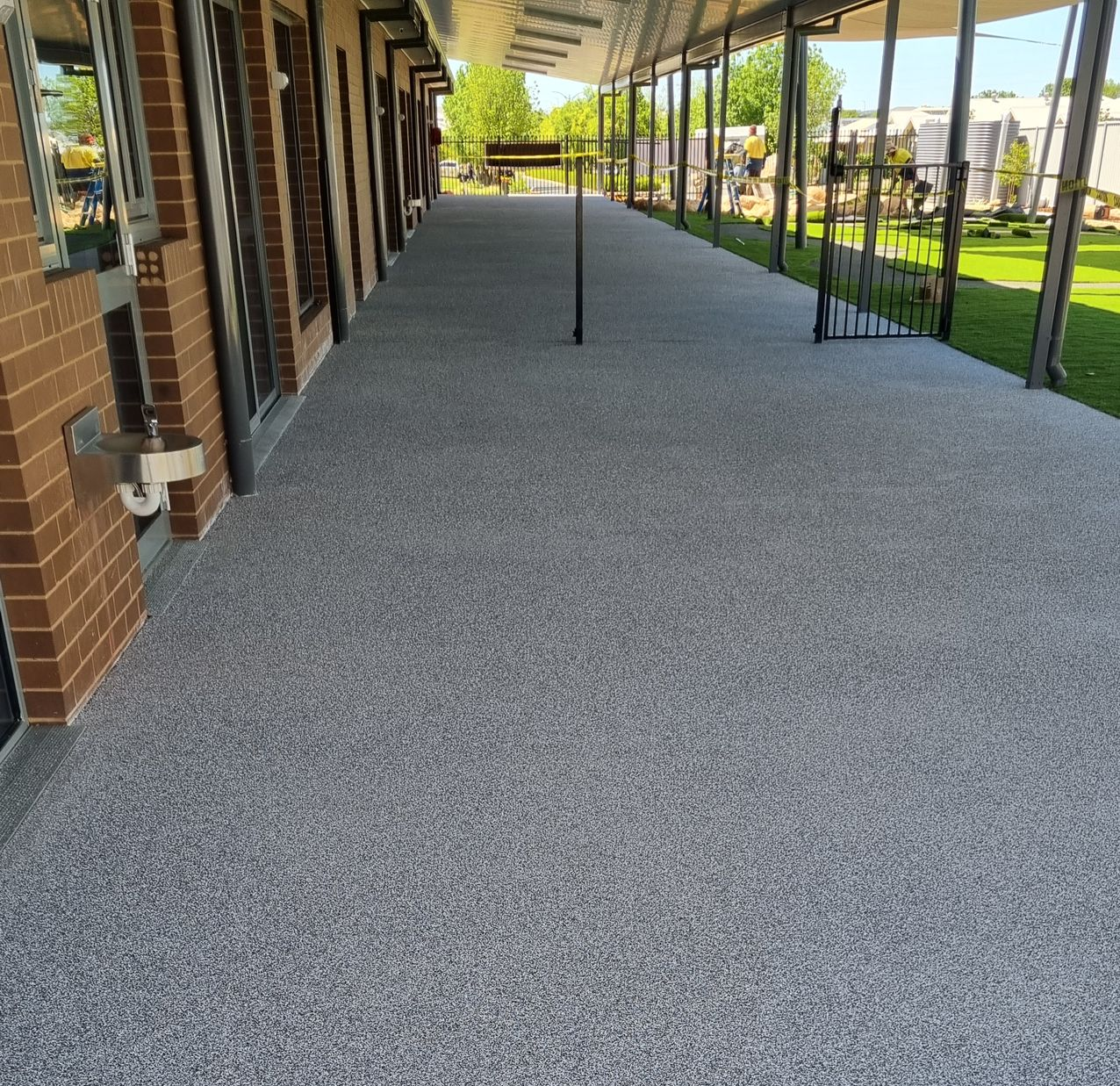 Covered outdoor walkway beside brick building with gray gravel surface and metal posts