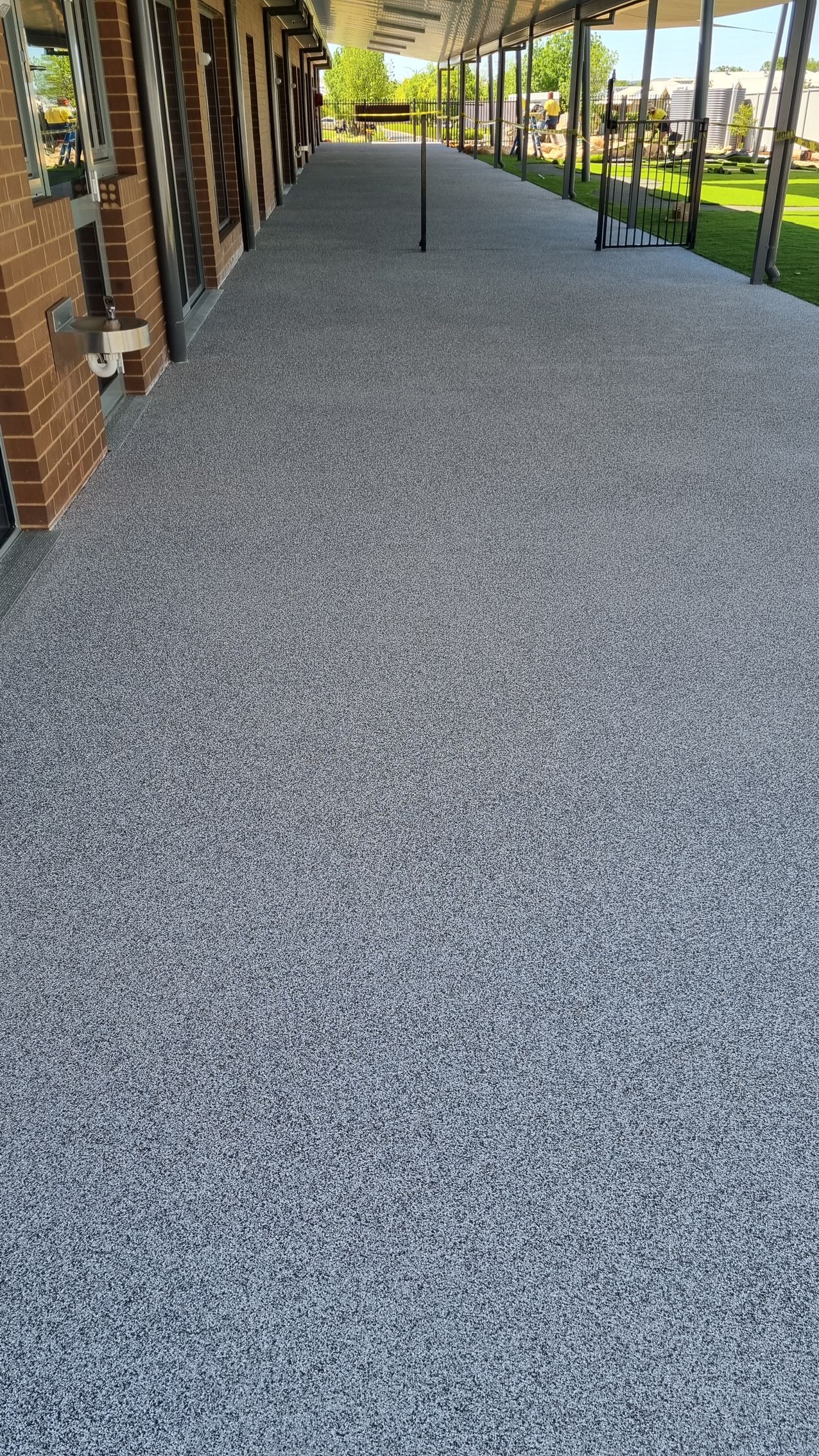 Covered walkway with gray gravel path beside brick storefronts and green lawn in the distance