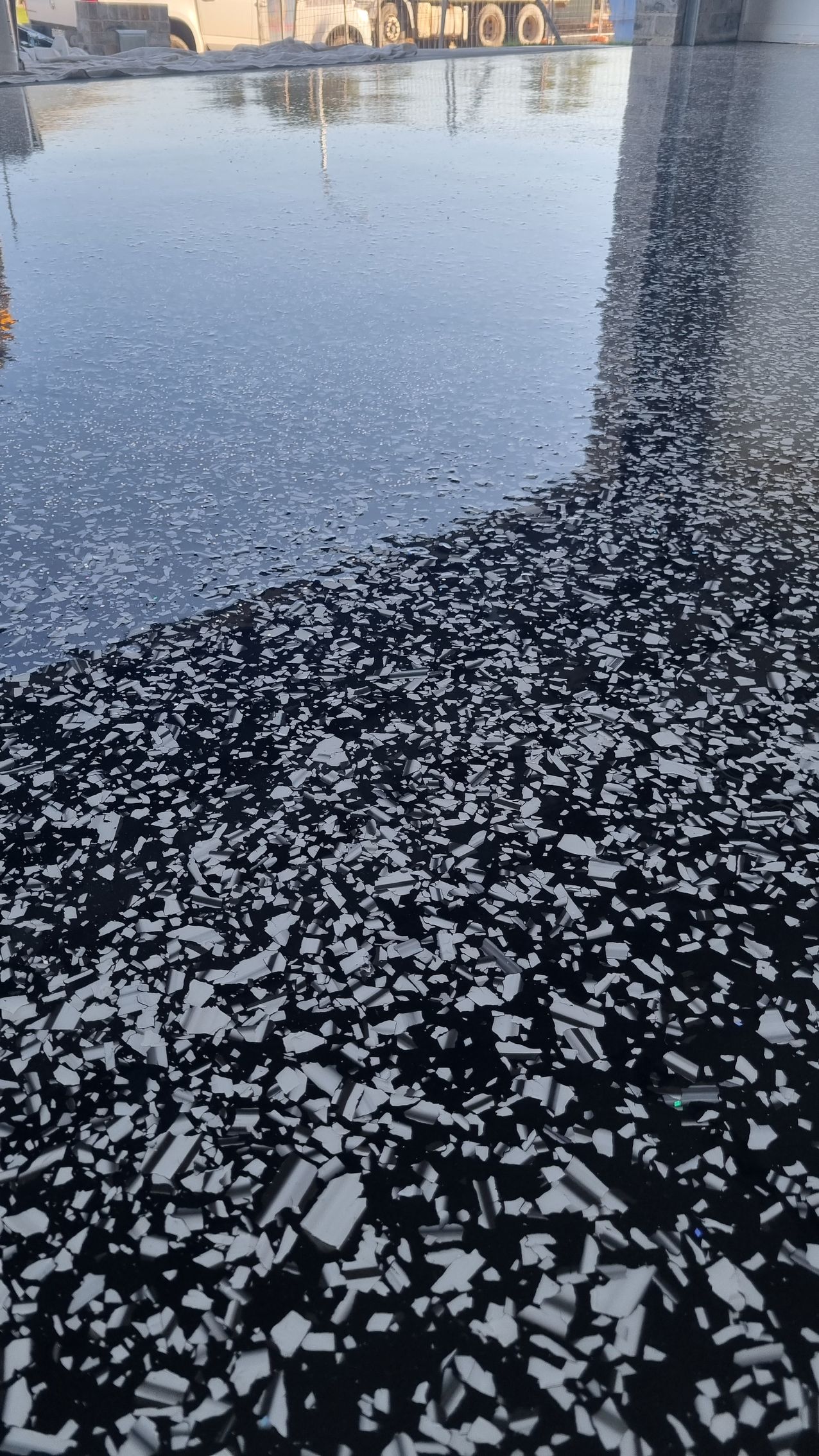 Frozen puddle beside dark speckled ground with a reflected building in the water