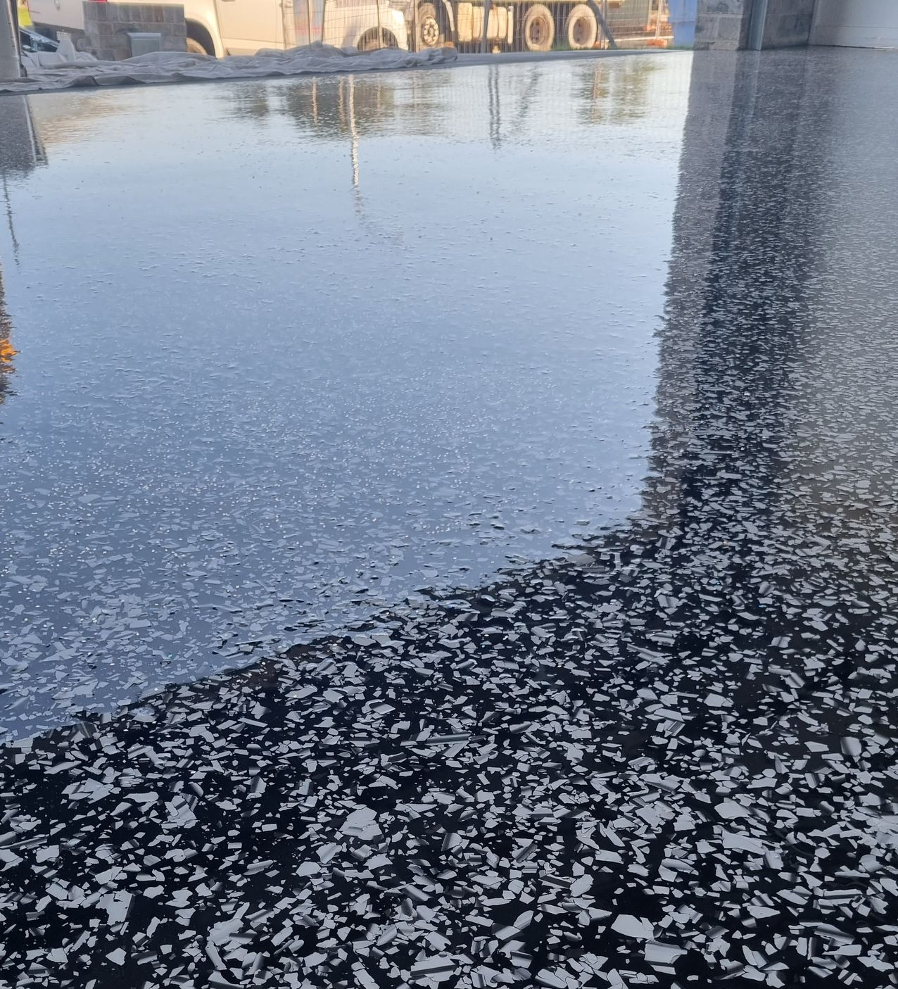 Icy puddle beside a snow-dusted road, reflecting buildings and a tree-lined horizon