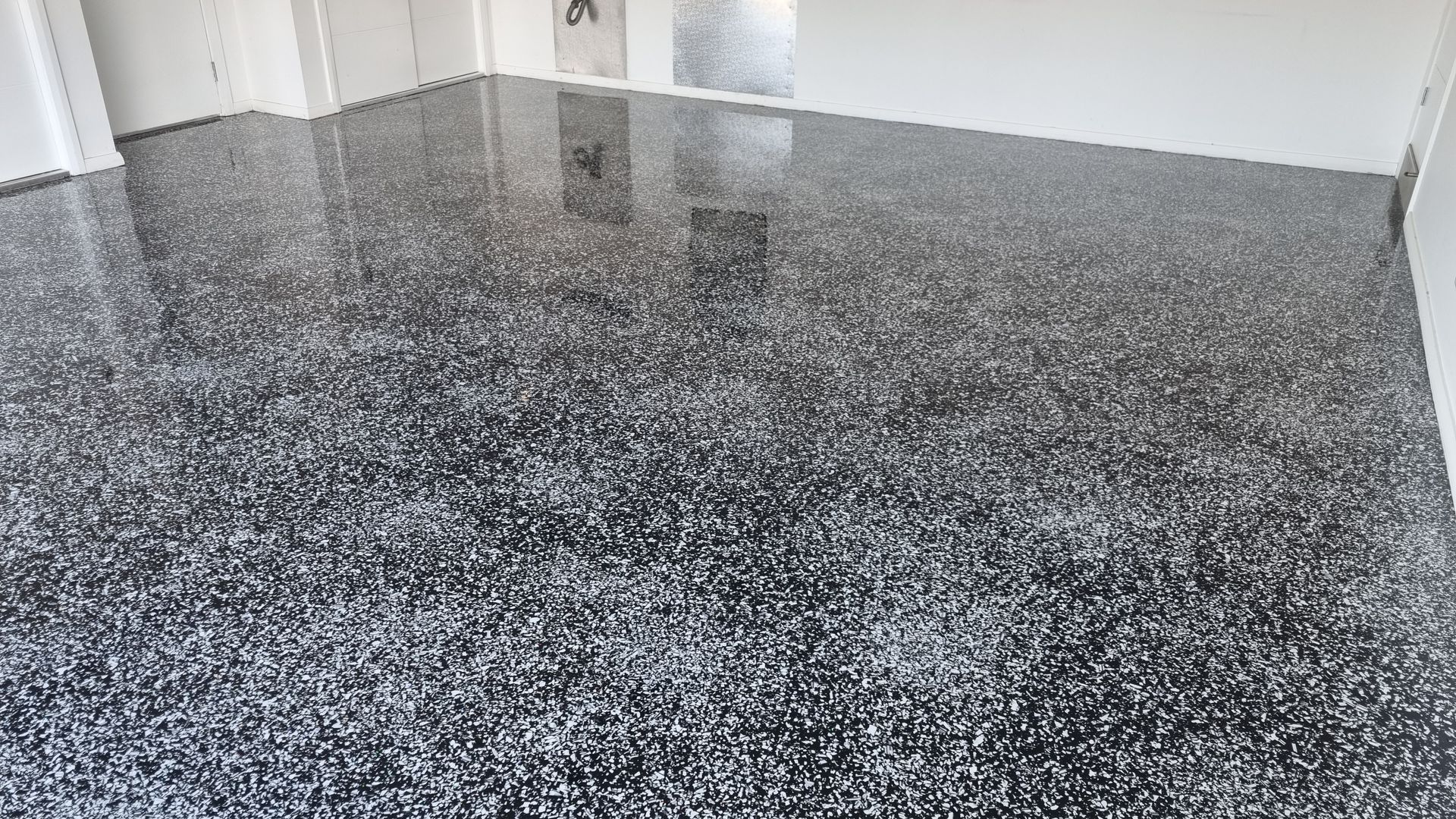 Empty room with glossy black-speckled floor and light-colored walls near a doorway