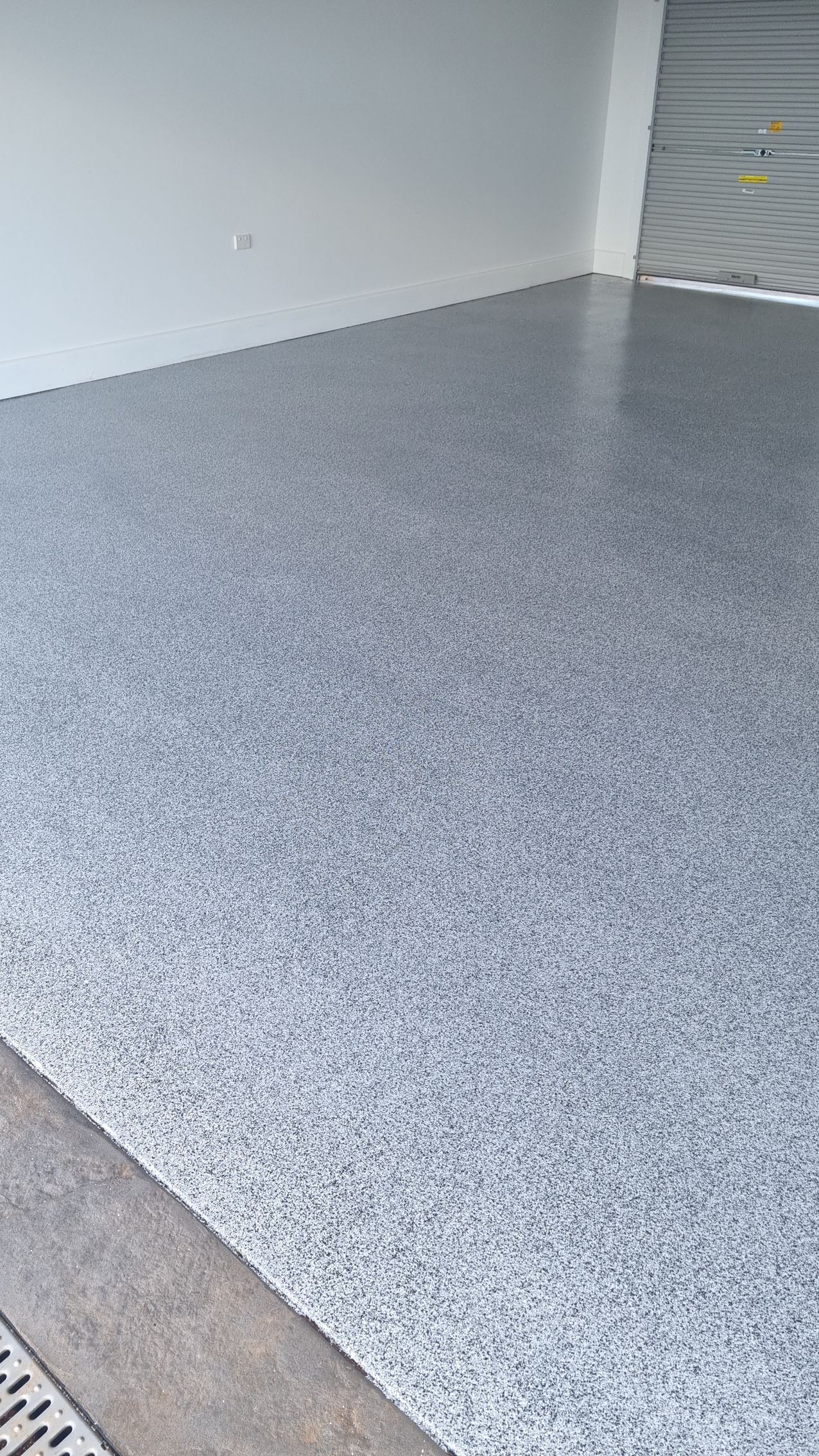 Speckled gray epoxy floor in a clean empty garage with white walls and a closed roll-up door