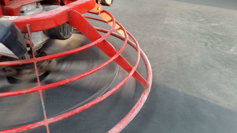 A Red Power Trowel With Spinning Blades Smoothes a Gray Concrete Floor — Western Epoxy Works In Dubbo, NSW