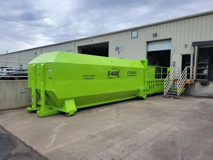 A large green dumpster is parked in front of a building.