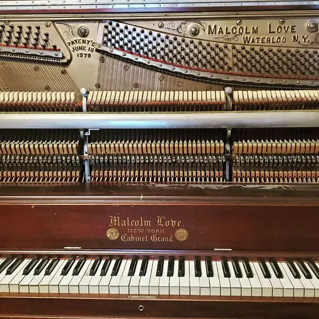 Open upright piano with exposed strings and hammers, labeled “Malcolm Love” and “Wolcott, N.Y.”