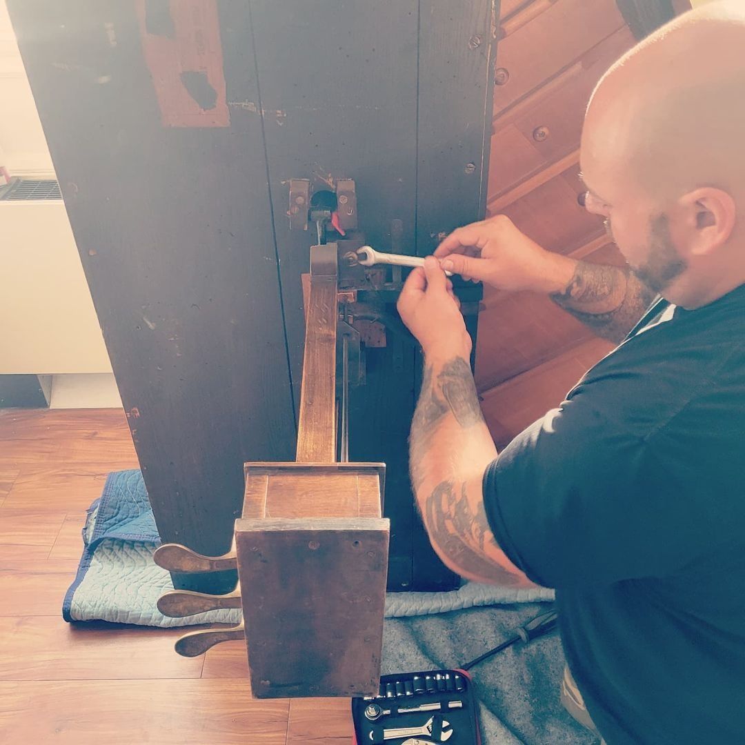 Person kneeling to repair a dark wooden chair with tools on a rug near a wooden wall