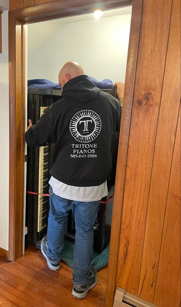 Person in a black jacket and jeans stands in a doorway, facing into a room with wood floors.