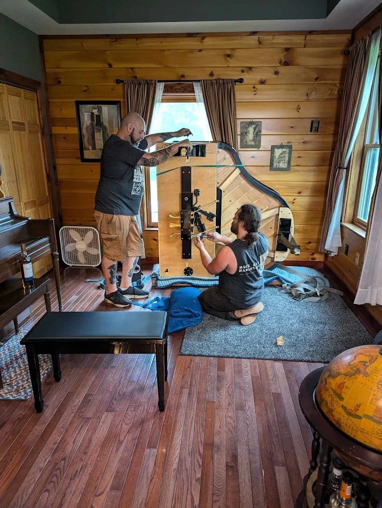 Two people assembling exercise equipment in a wood-paneled living room with a mirror and benches