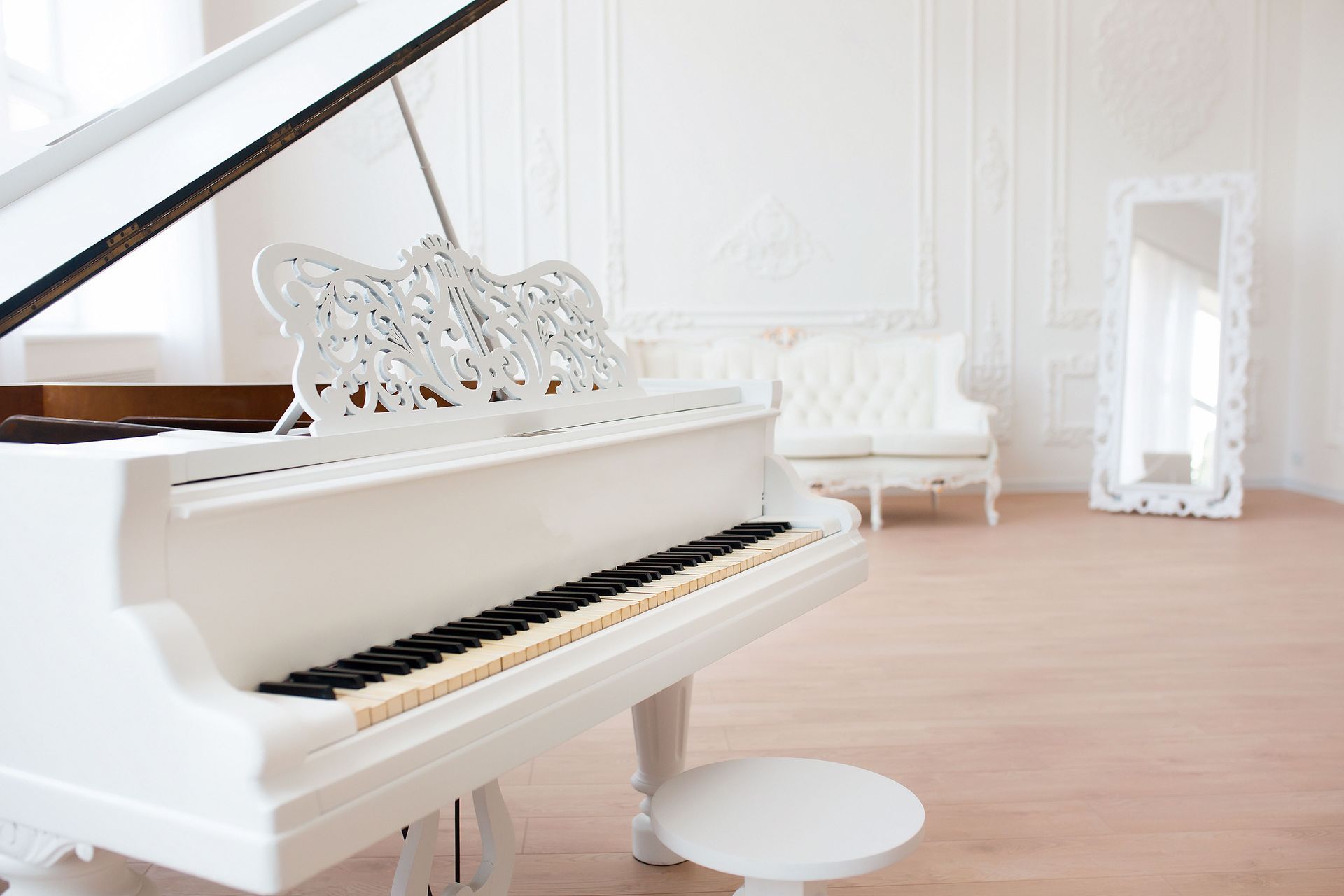 White grand piano in a bright room with a matching bench and ornate decor