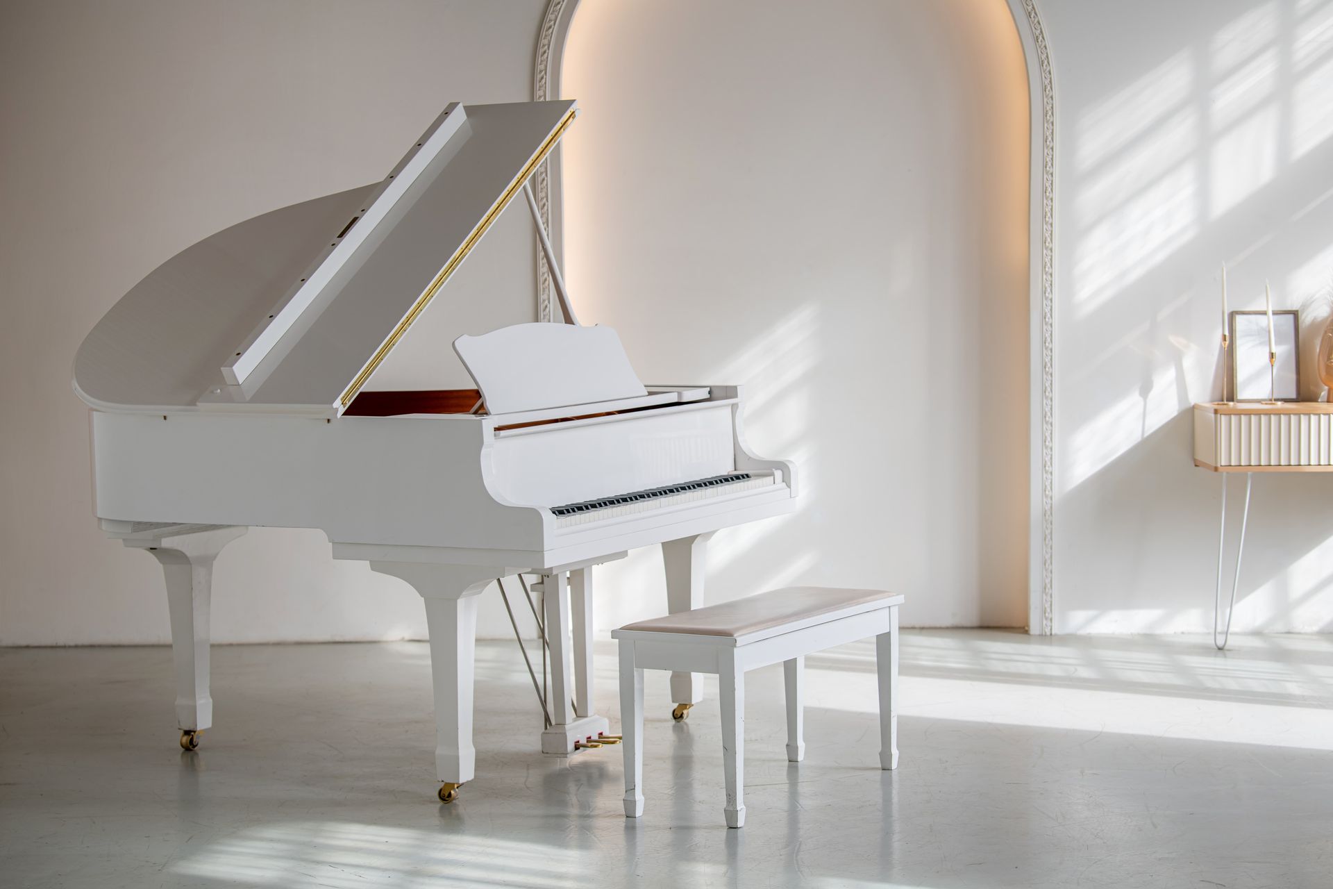 White grand piano and bench in a bright minimalist room with an arched doorway.