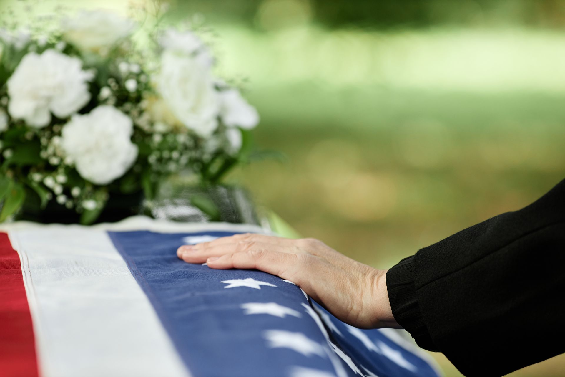 A woman is holding an american flag and a rose at a funeral.
