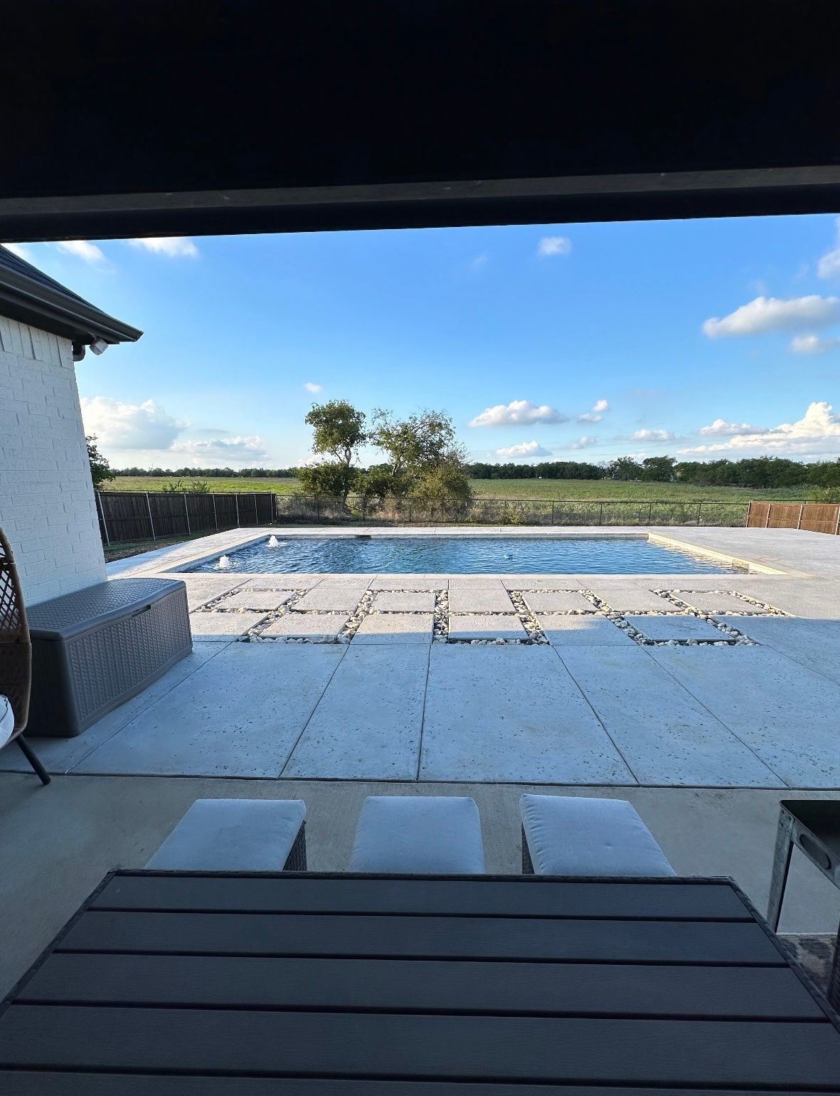 A view of a swimming pool from a patio with a table and chairs.