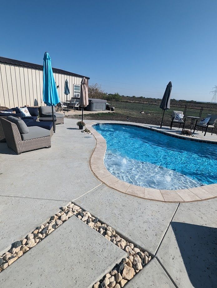 A large swimming pool is surrounded by patio furniture and umbrellas.