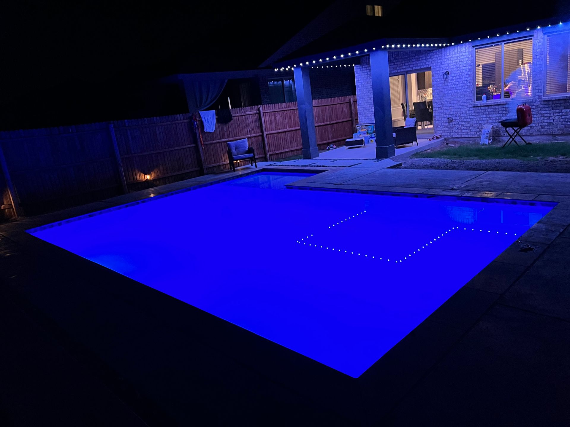 A large swimming pool is lit up with blue lights at night.