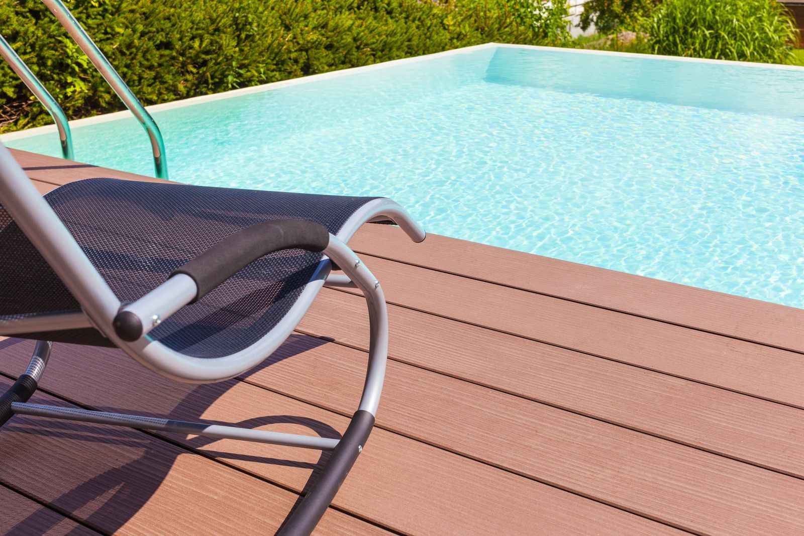 A view of a swimming pool from a patio with a table and chairs.