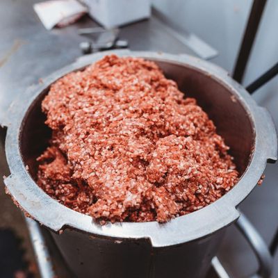 A metal bowl filled with ground meat is on a table A metal bowl filled with ground meat is on a table