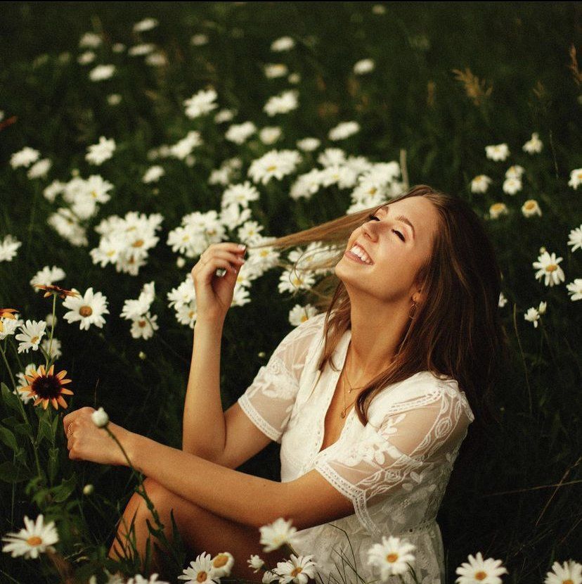 Woman in a white dress smiling among white daisies in a grassy field
