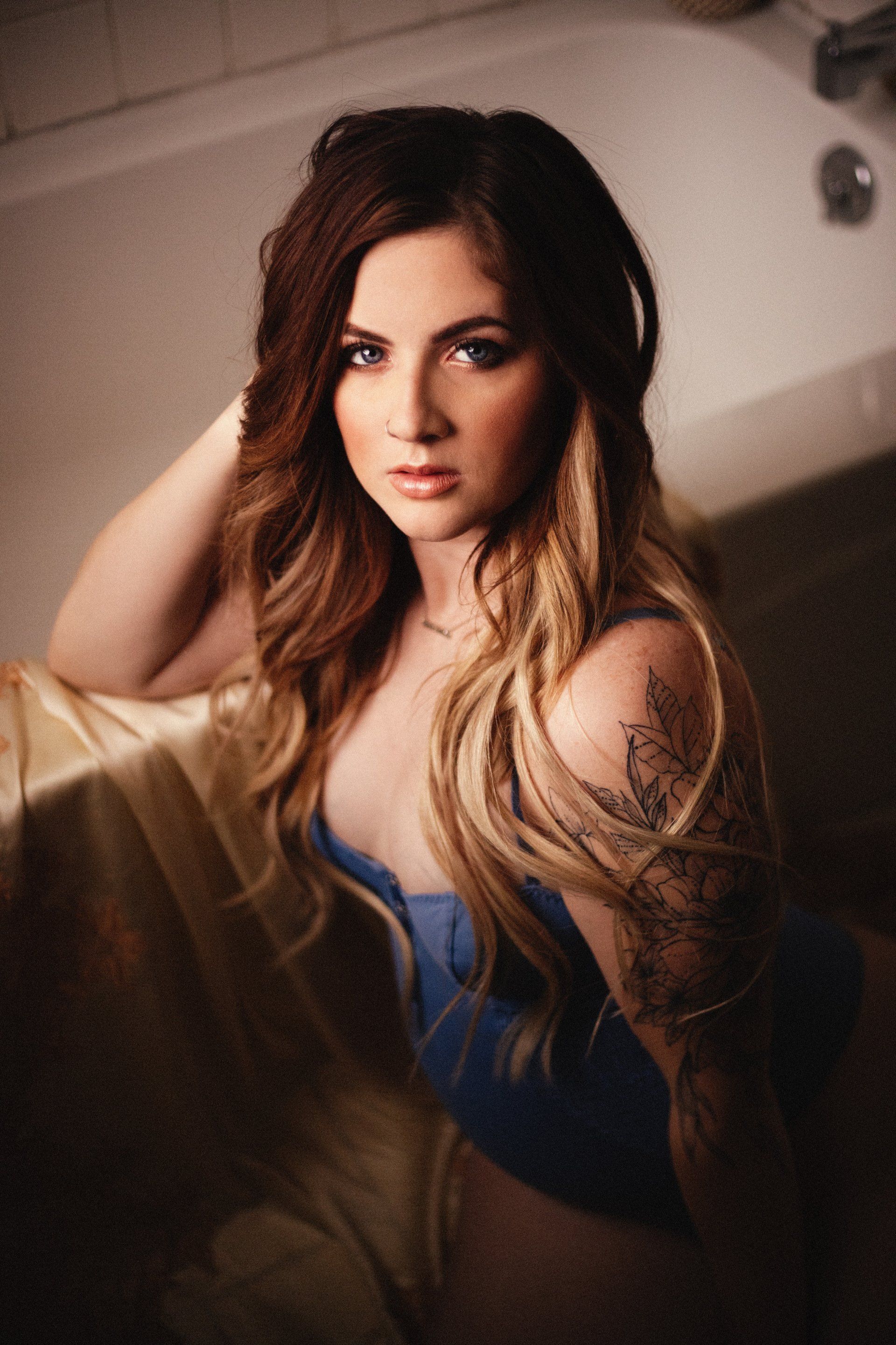 Woman in a blue top sitting on a bed, looking at the camera.