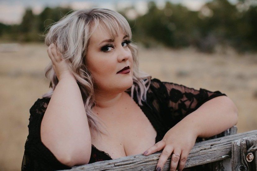 Portrait of a woman leaning on a wooden fence in a field, wearing a black lace top