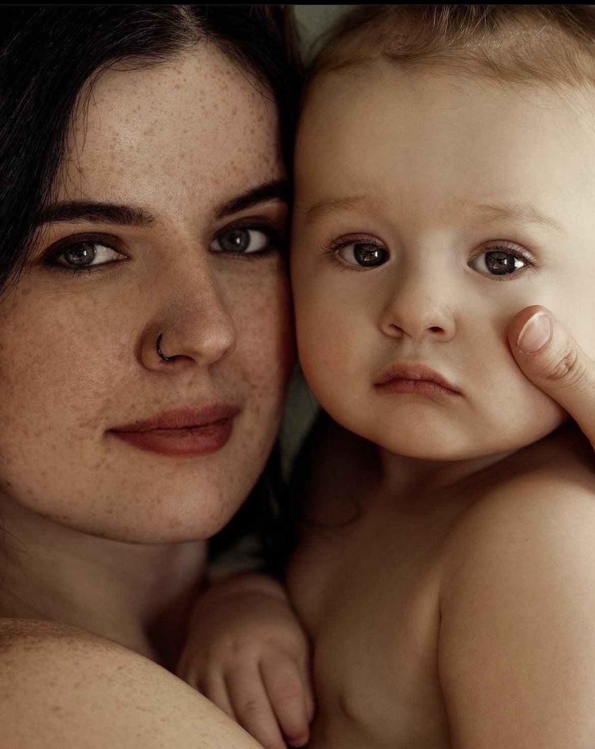 Close-up of a woman holding a baby, both looking at the camera.