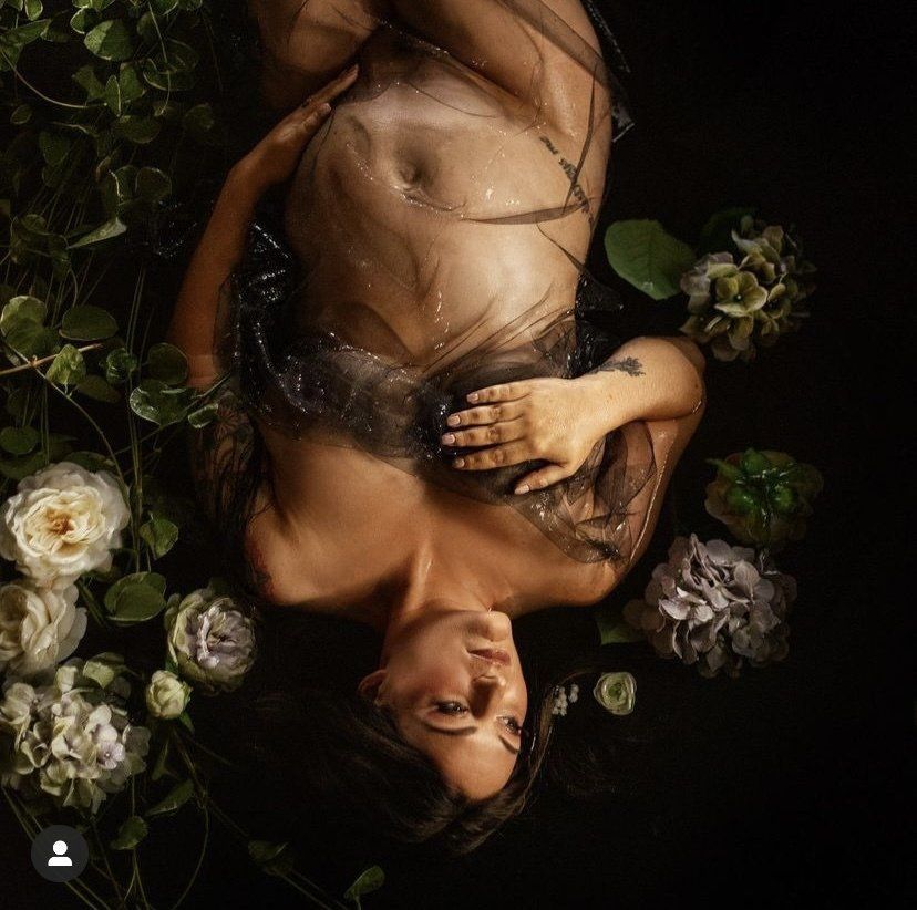Upward view of a nude person lying among white flowers and dark green leaves in low light