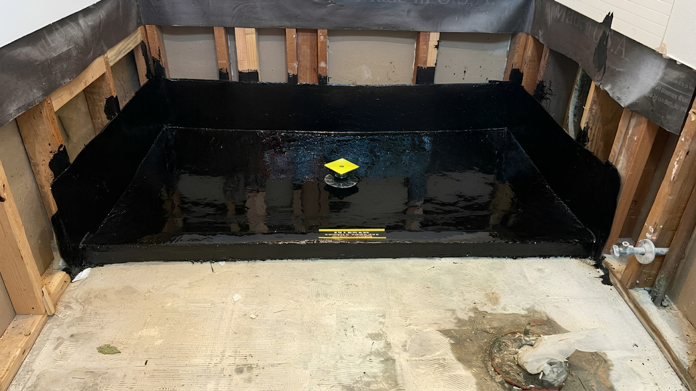 Partially flooded room with a black waterproofed wall and shallow standing water on the floor