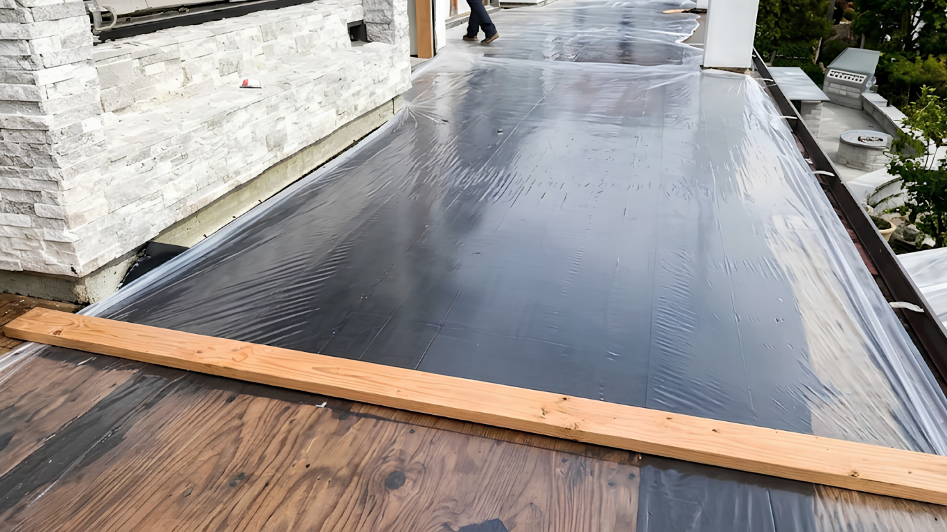 Rain-soaked rooftop walkway with dark waterproof membrane and wooden plank near a stone wall