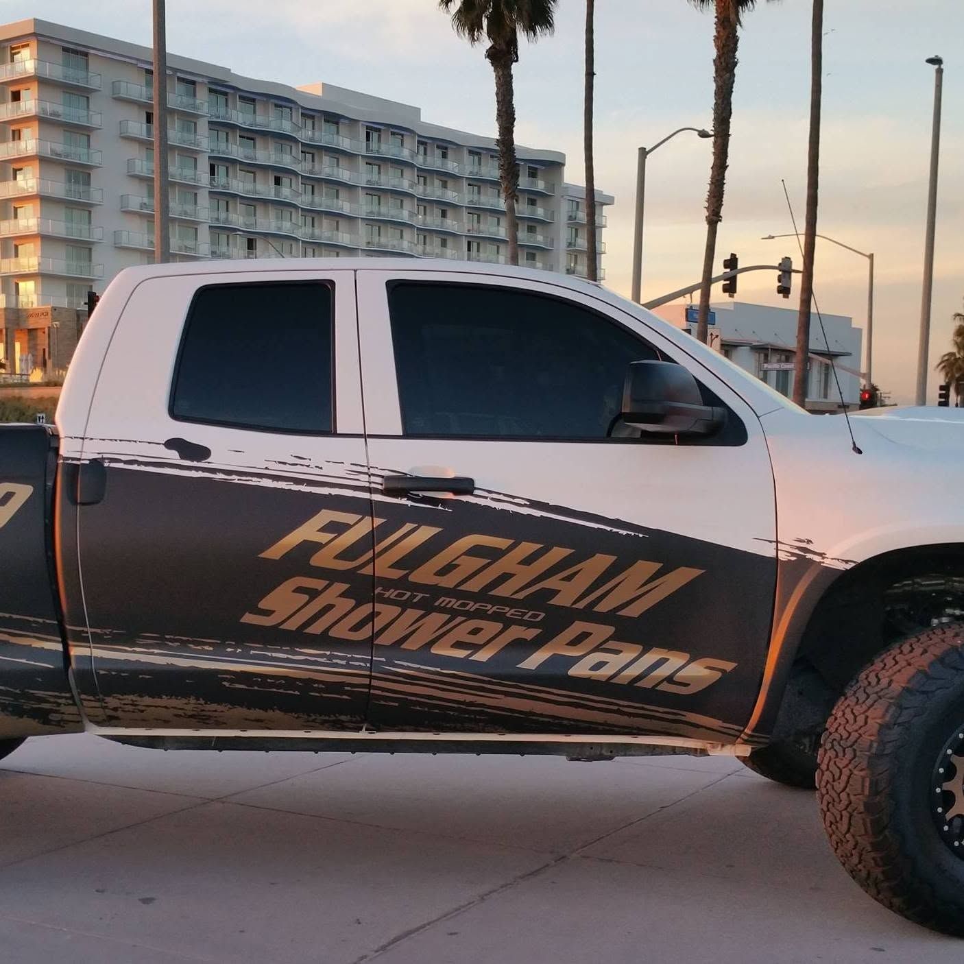 White lifted pickup with “Fulgham Shower Plans” branding parked near the beach at sunset