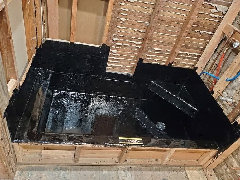 Black waterproofed floor in an unfinished bathroom framed with exposed wooden studs