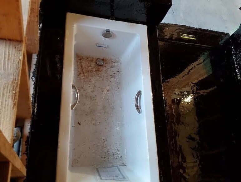 White bathtub filled with dirt and debris beside a dark, wet floor surface