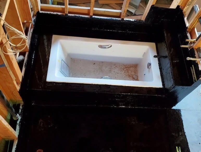 White bathtub set into a black tiled bathroom surround with a partially open wooden door.