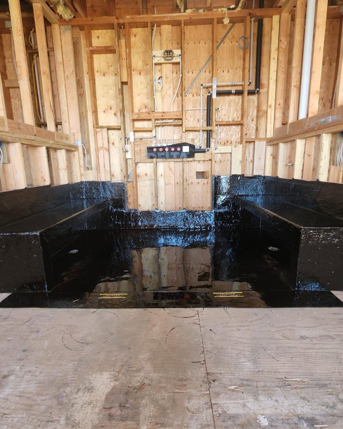 Black waterproofed built-in bench seating in a wooden-framed room under construction