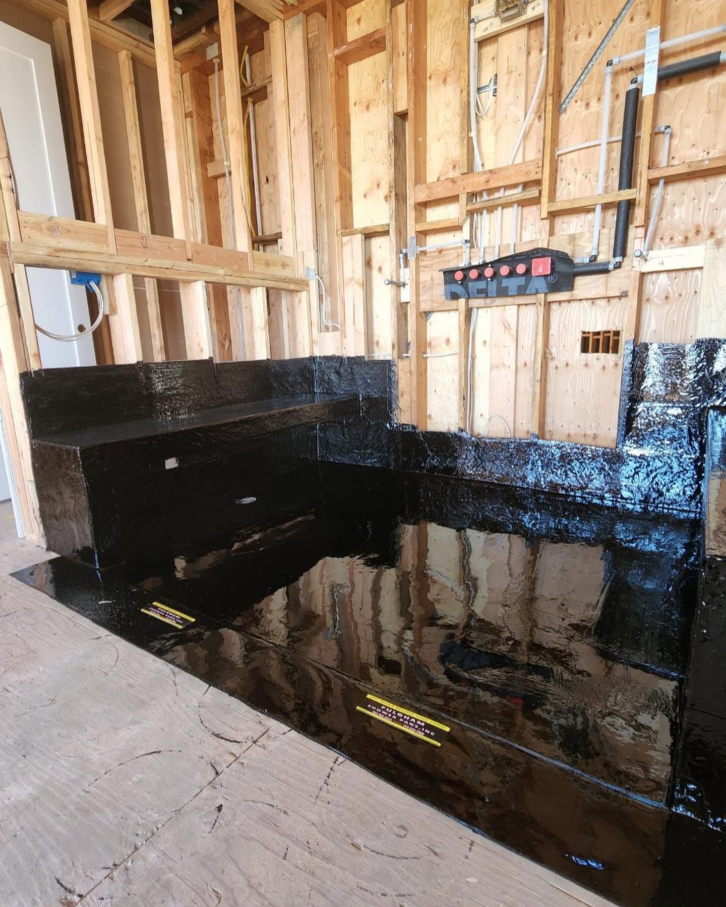 Unfinished basement with black waterproofed walls, exposed studs, and a flooded floor reflecting the framing.