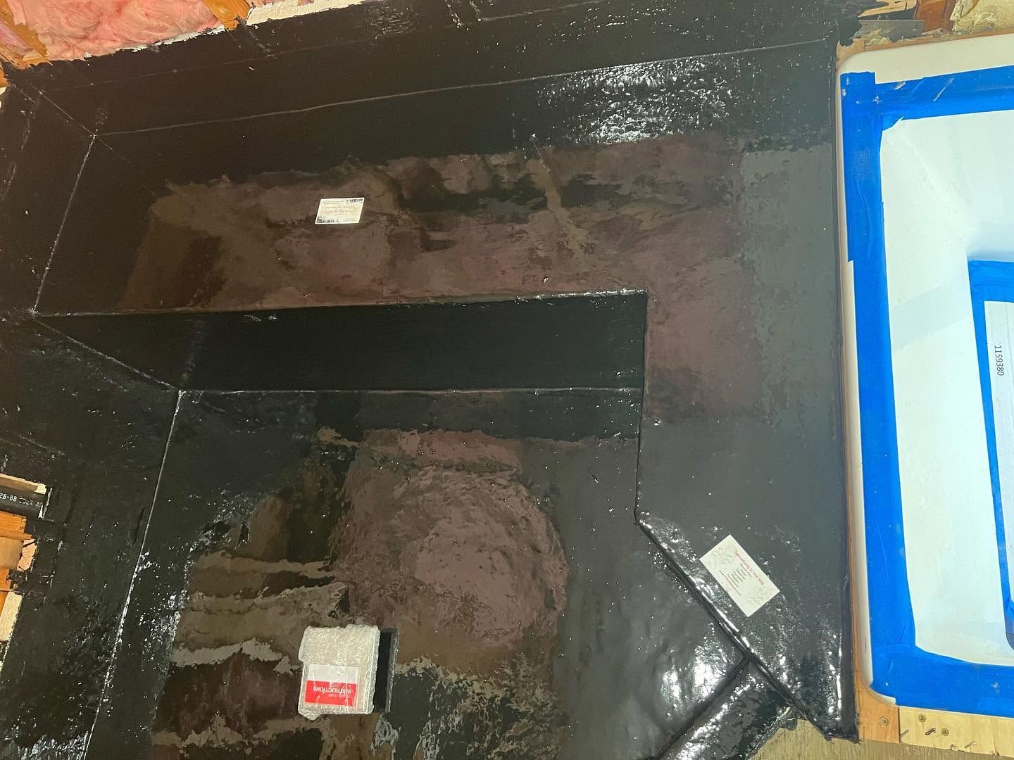 Black rectangular opening in a dark wall, with blue tape on the right and debris inside.