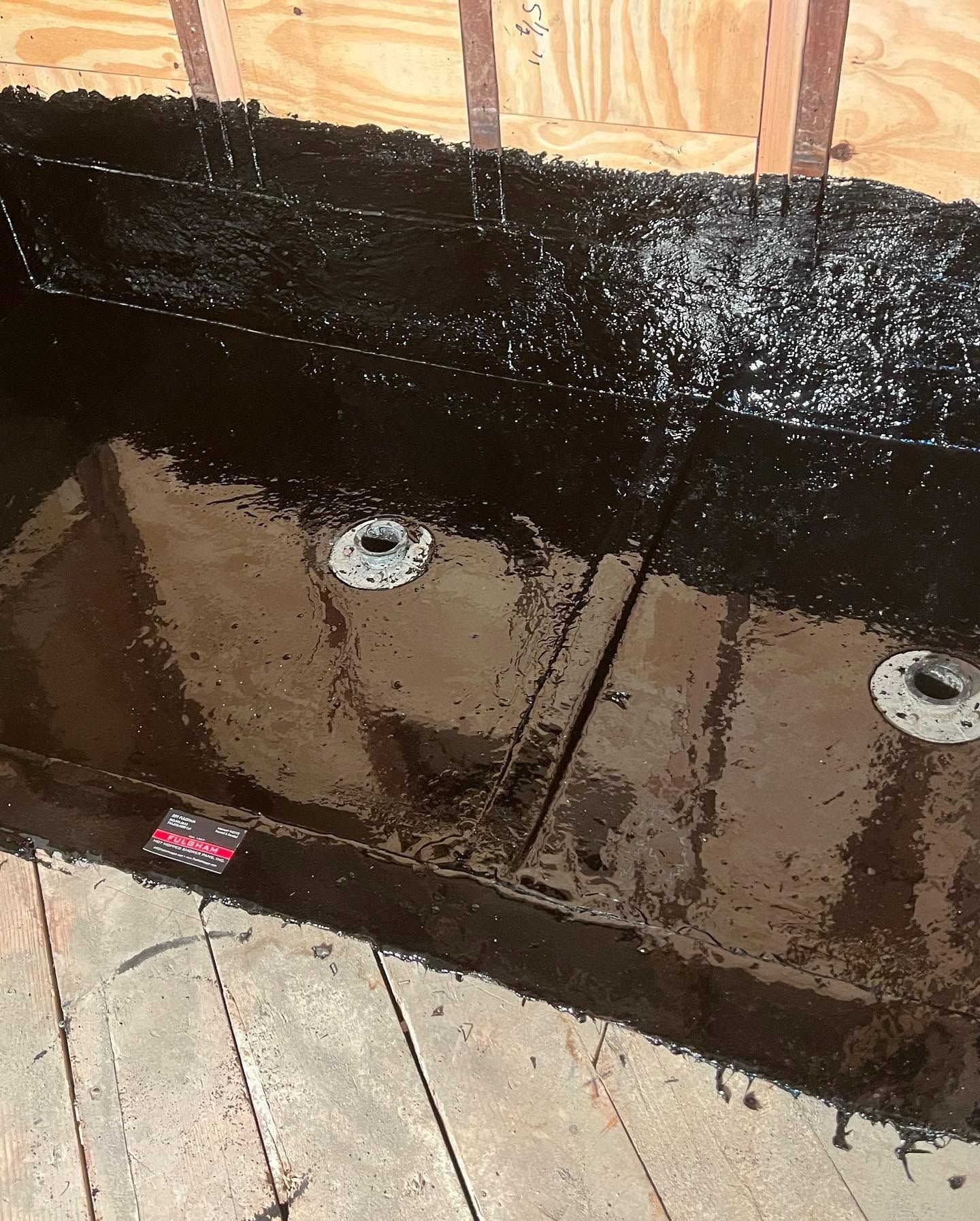 Black waterproofing membrane on plywood with two circular drain fittings near the bottom edge.