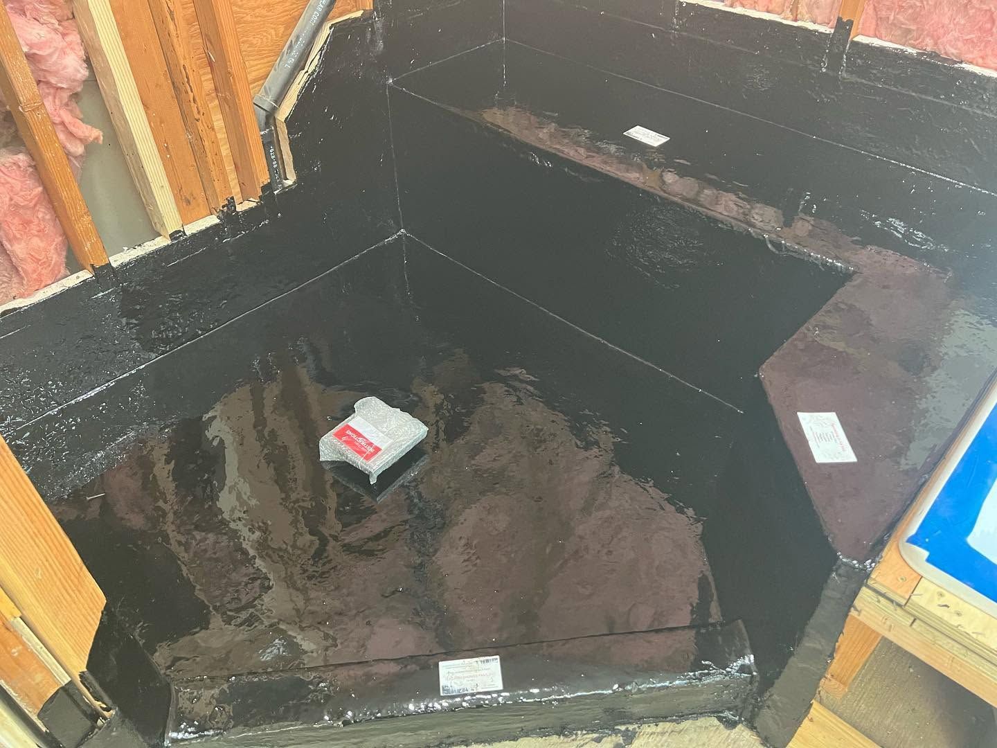 Black waterproofed corner pit with a small box inside, surrounded by insulation and wood framing.
