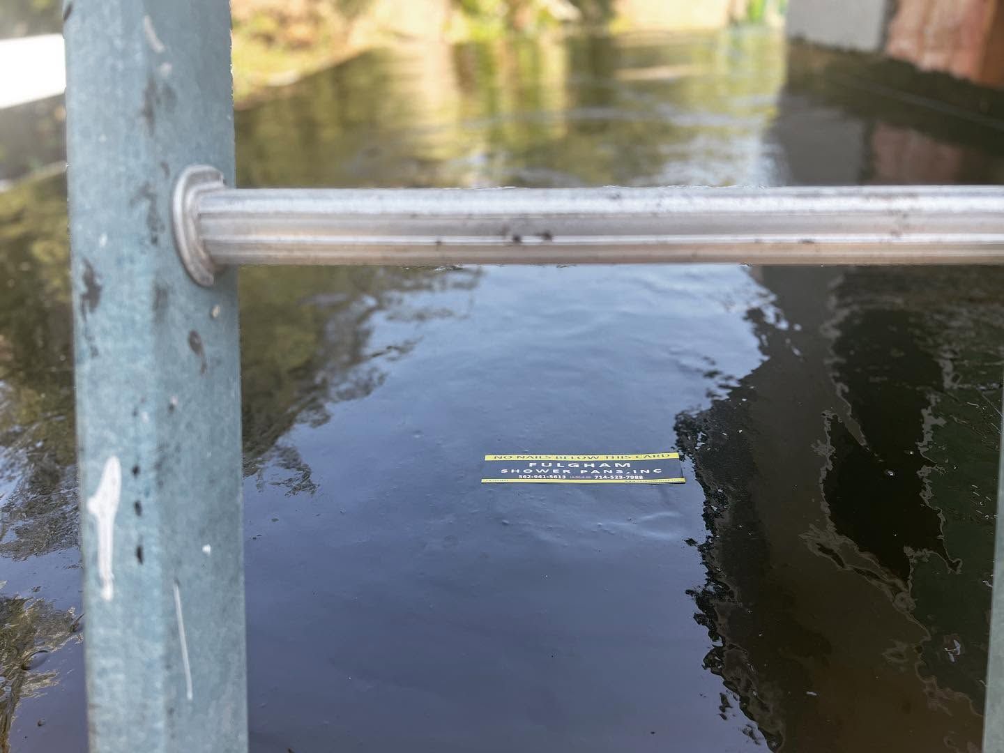 Metal rail over dark water beside a concrete post, with reflections of trees.