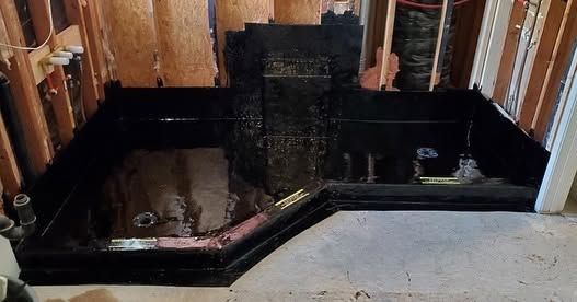 Black stone fireplace under construction in an unfinished room with exposed wooden framing.