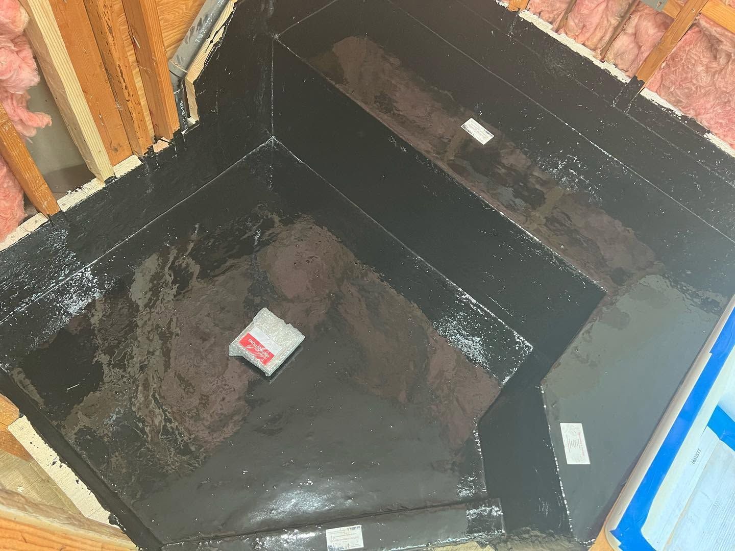 Dark unfinished basement corner with a recessed pit lined in black tar paper and exposed framing.