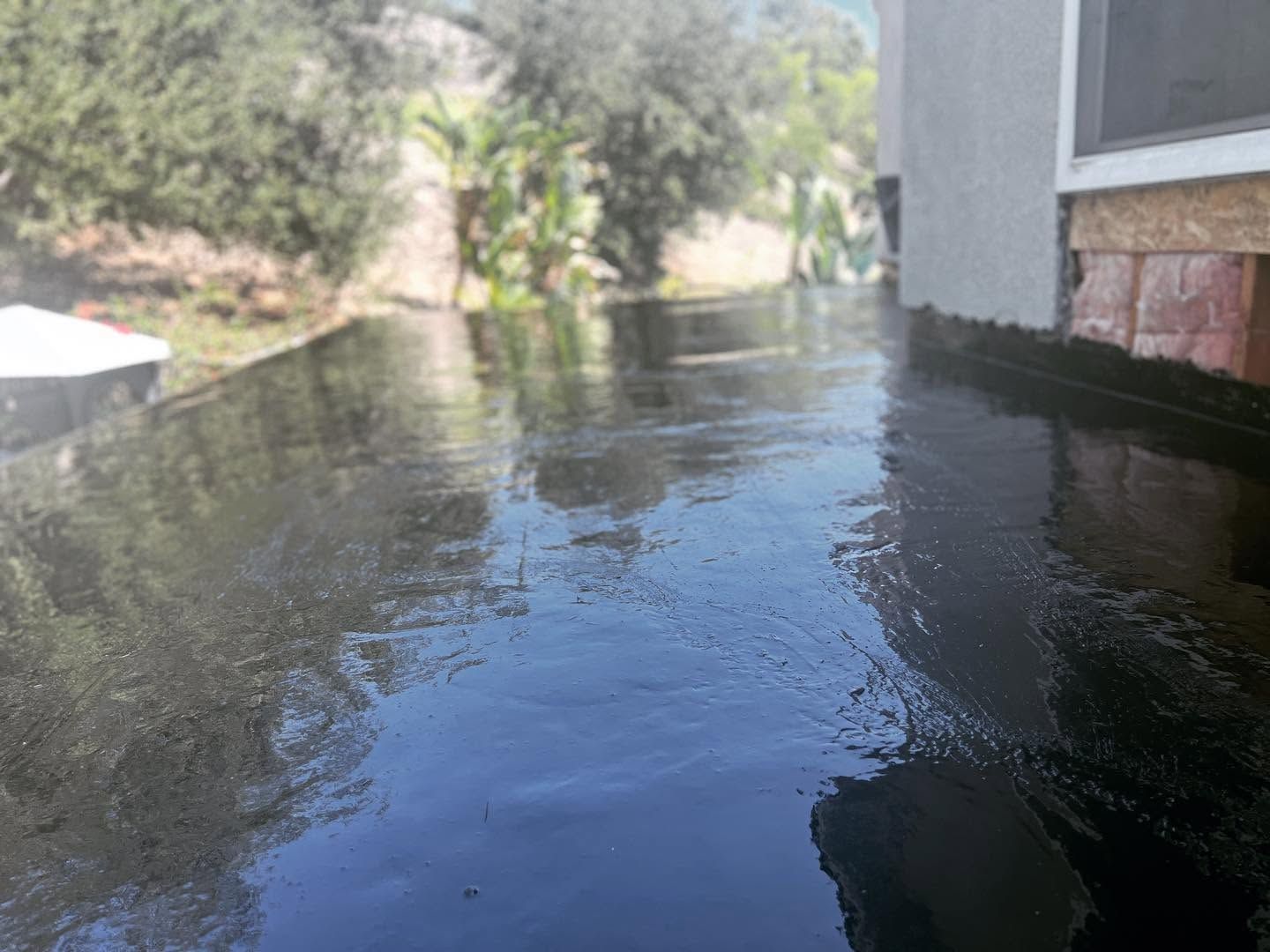 Floodwater reflecting a building beside a narrow creek, with trees along the banks