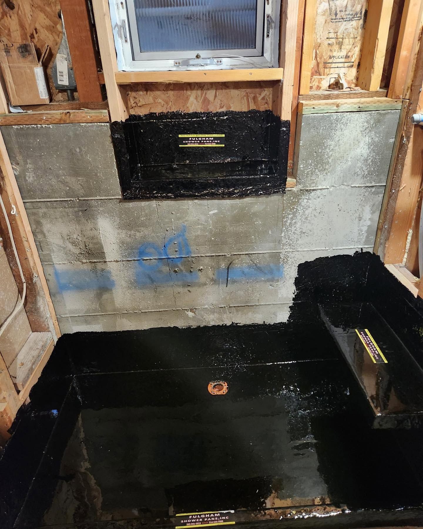 Basement wall with black waterproofing membrane and a small window above unfinished concrete floor
