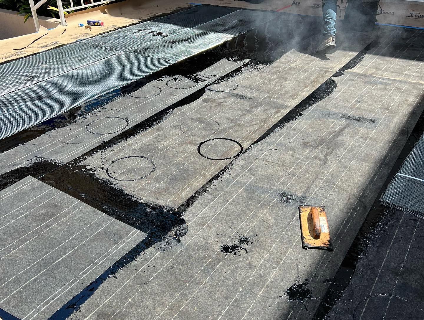 Damaged flat roof with torn black membrane, exposed patching, and a small tool on the surface