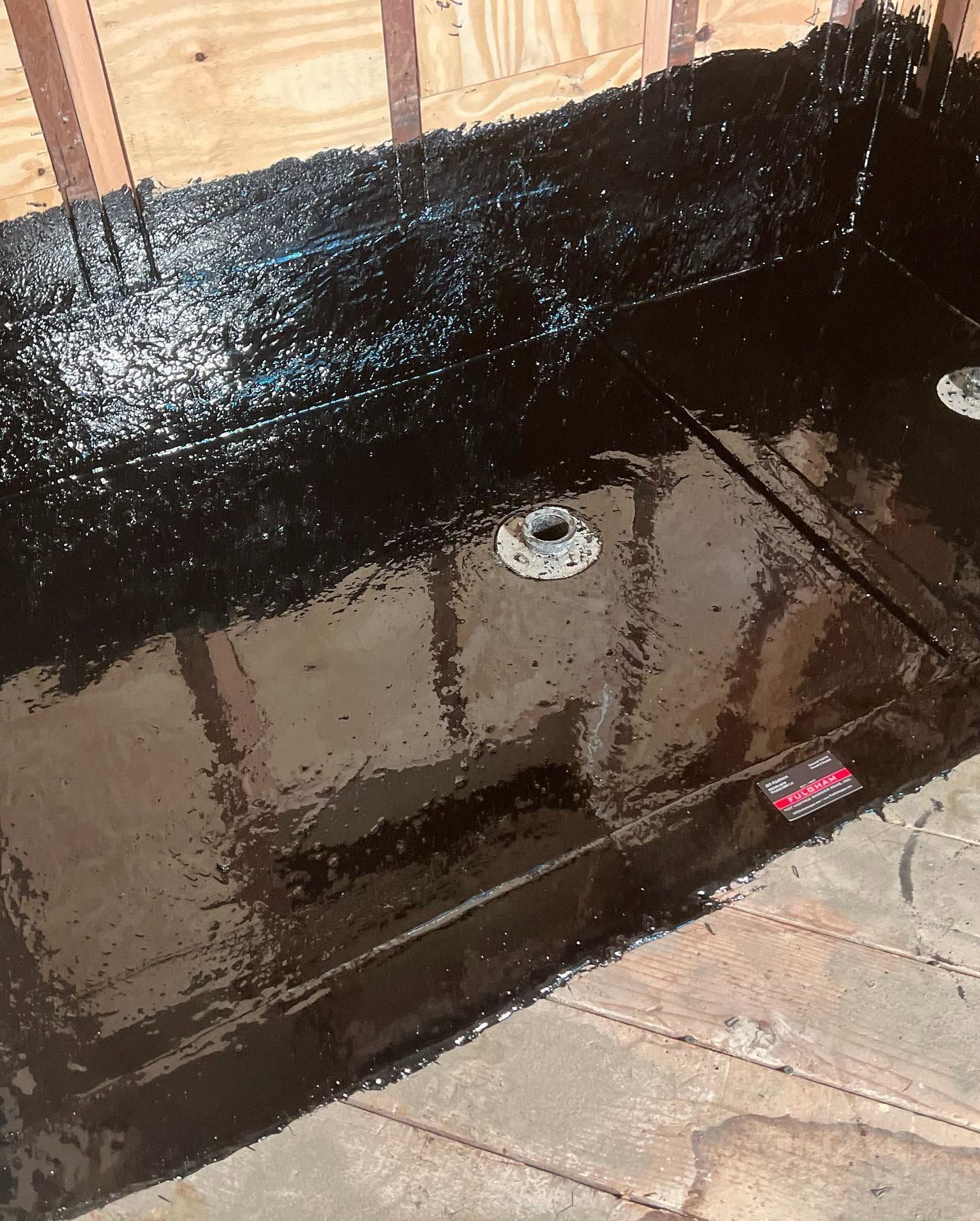 Black waterproofed shower pan with a drain in a tiled bathroom under construction