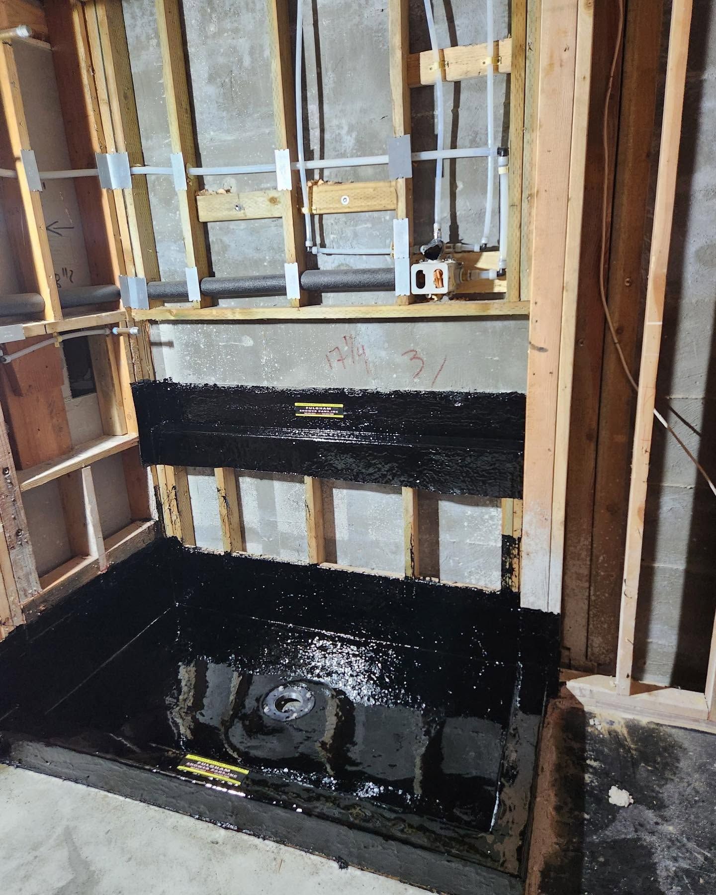 Partially built shower alcove with black waterproofing and exposed wall studs