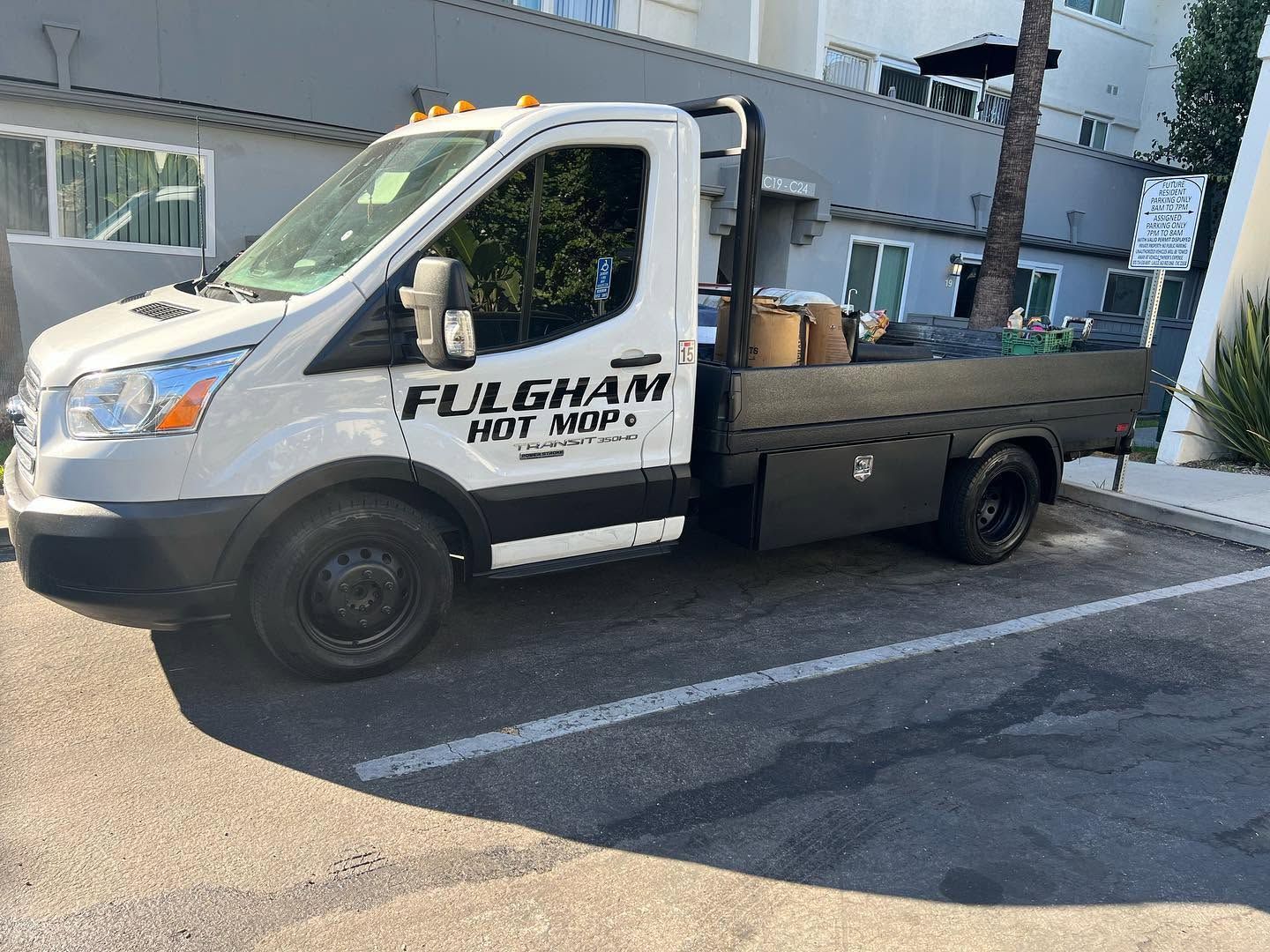 White utility truck parked on a street beside a building, with black flatbed and cab logo.
