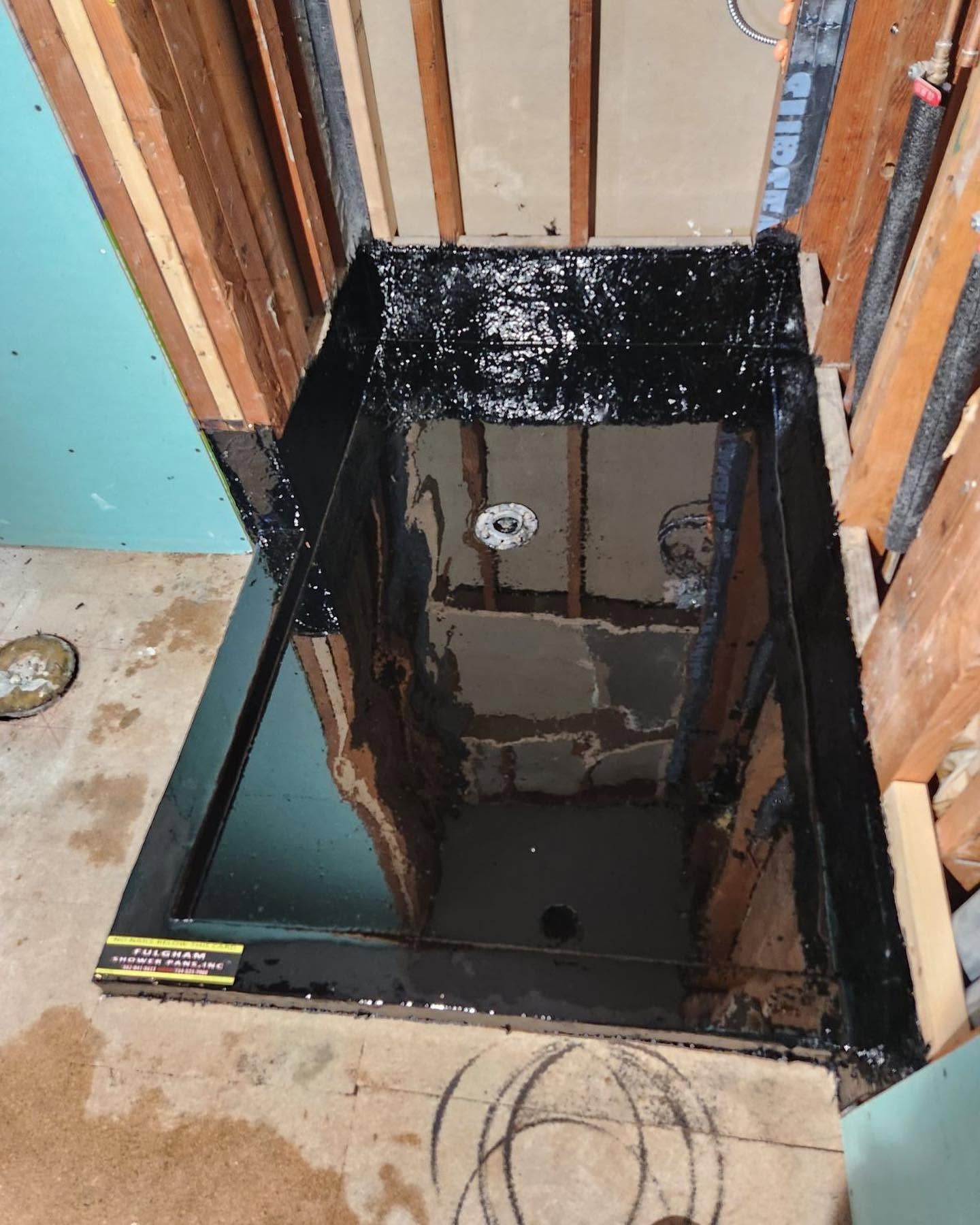 Black waterproof-lined shower pan with drain in a partially finished bathroom/closet space
