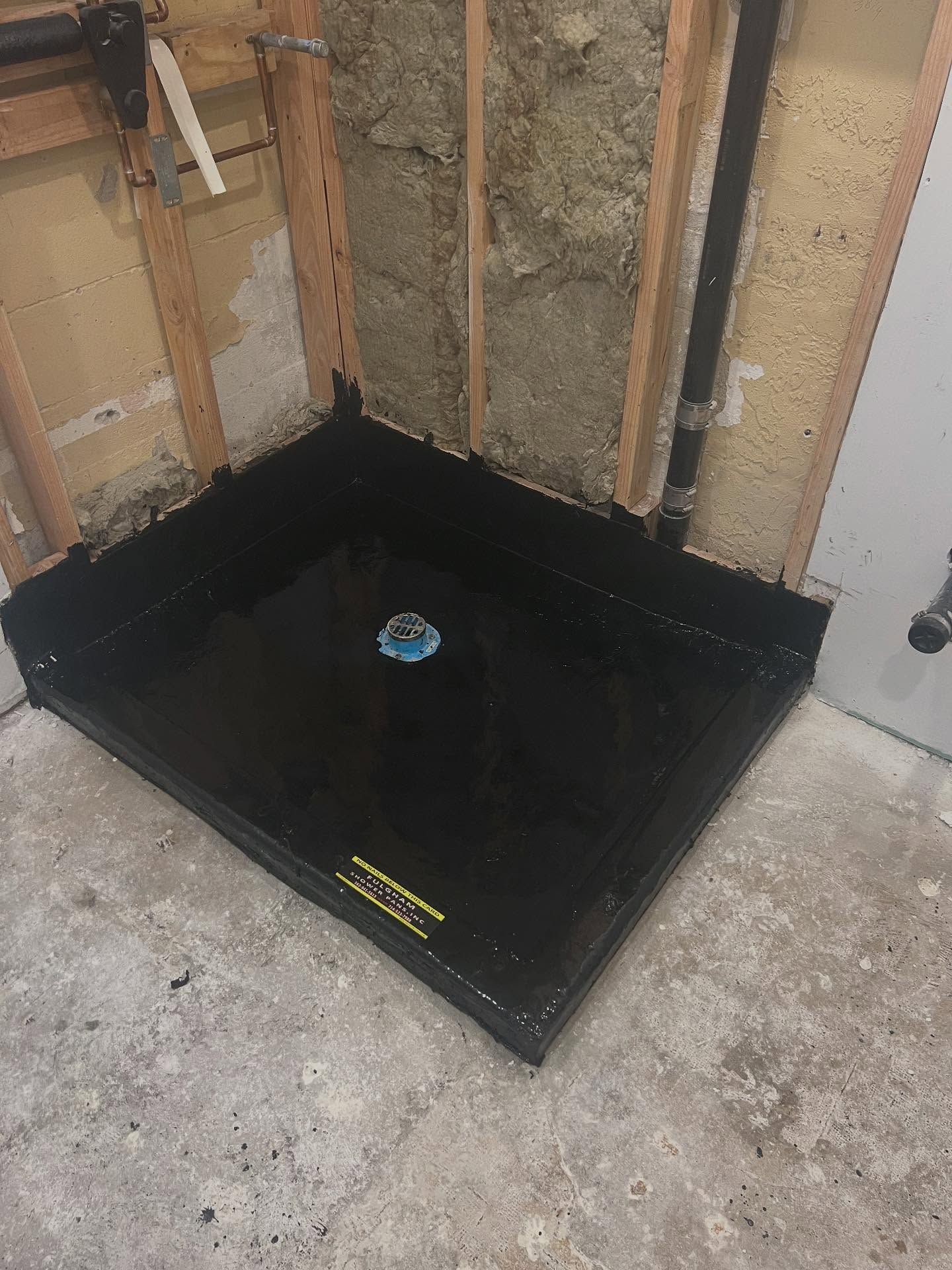 Black waterproof shower pan installed at the base of unfinished bathroom walls.