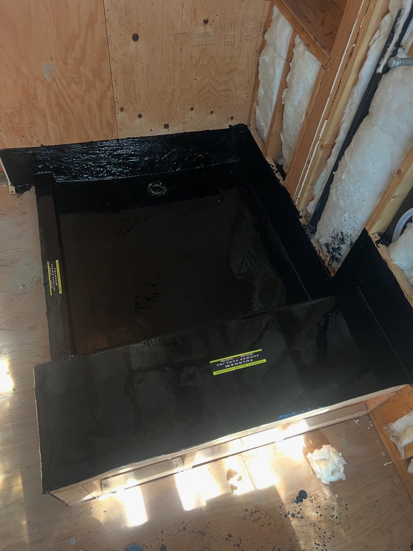 Black waterproofed square pit or floor opening inside unfinished wooden framing.