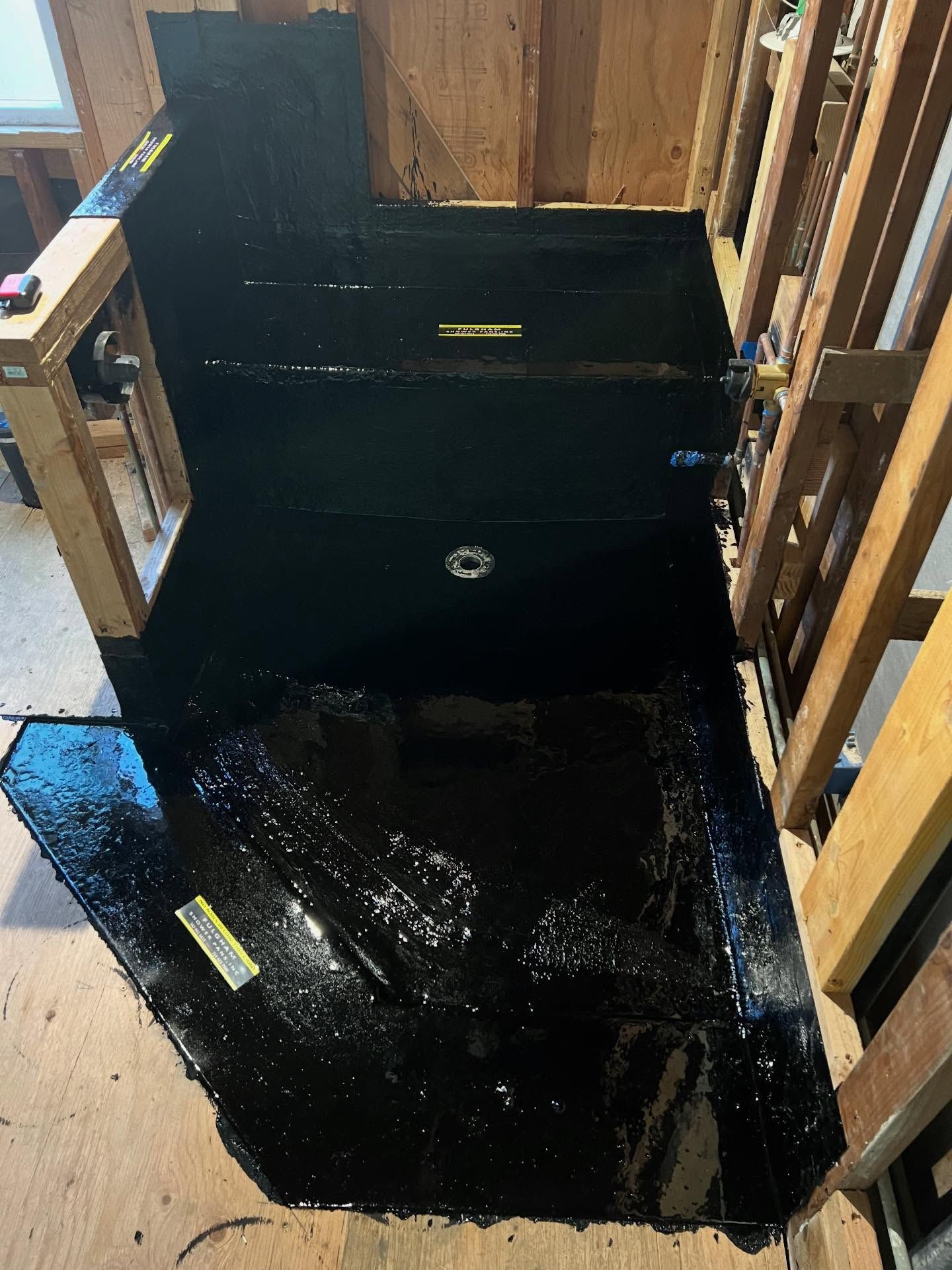 Large black waterproof liner inside a wooden-framed stairwell or trench opening indoors