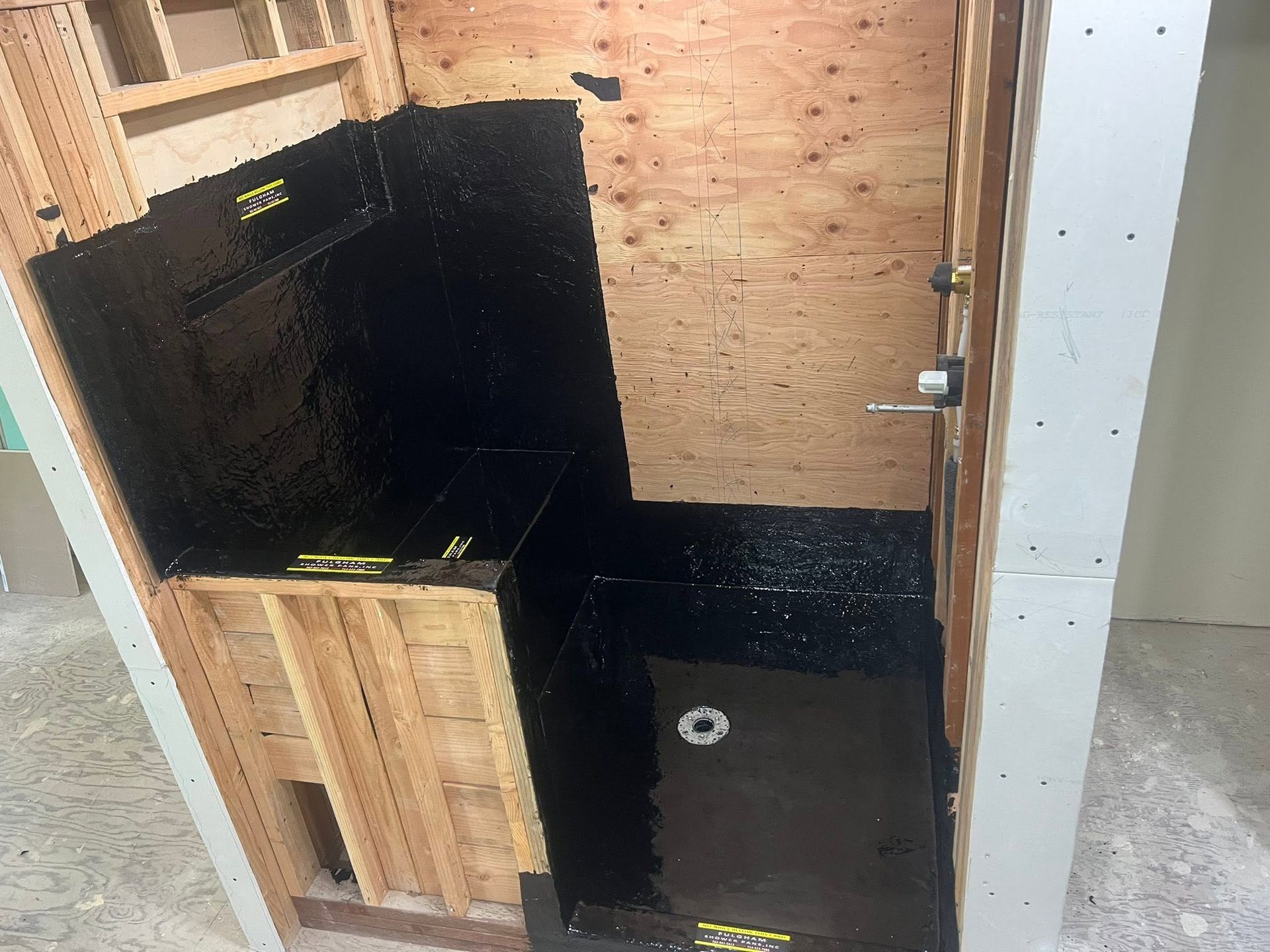 Partially built shower stall with black waterproof panels and unfinished wood framing
